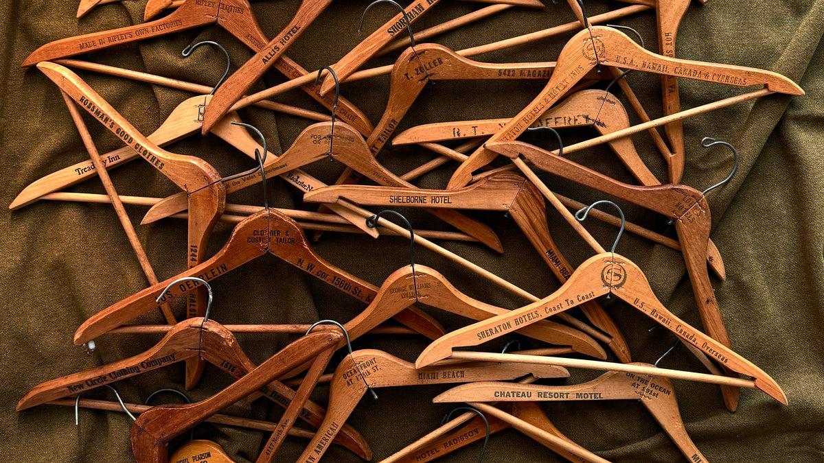 A pile of personalized wooden hangers with engraved names and dates, arranged on a dark olive green fabric background.